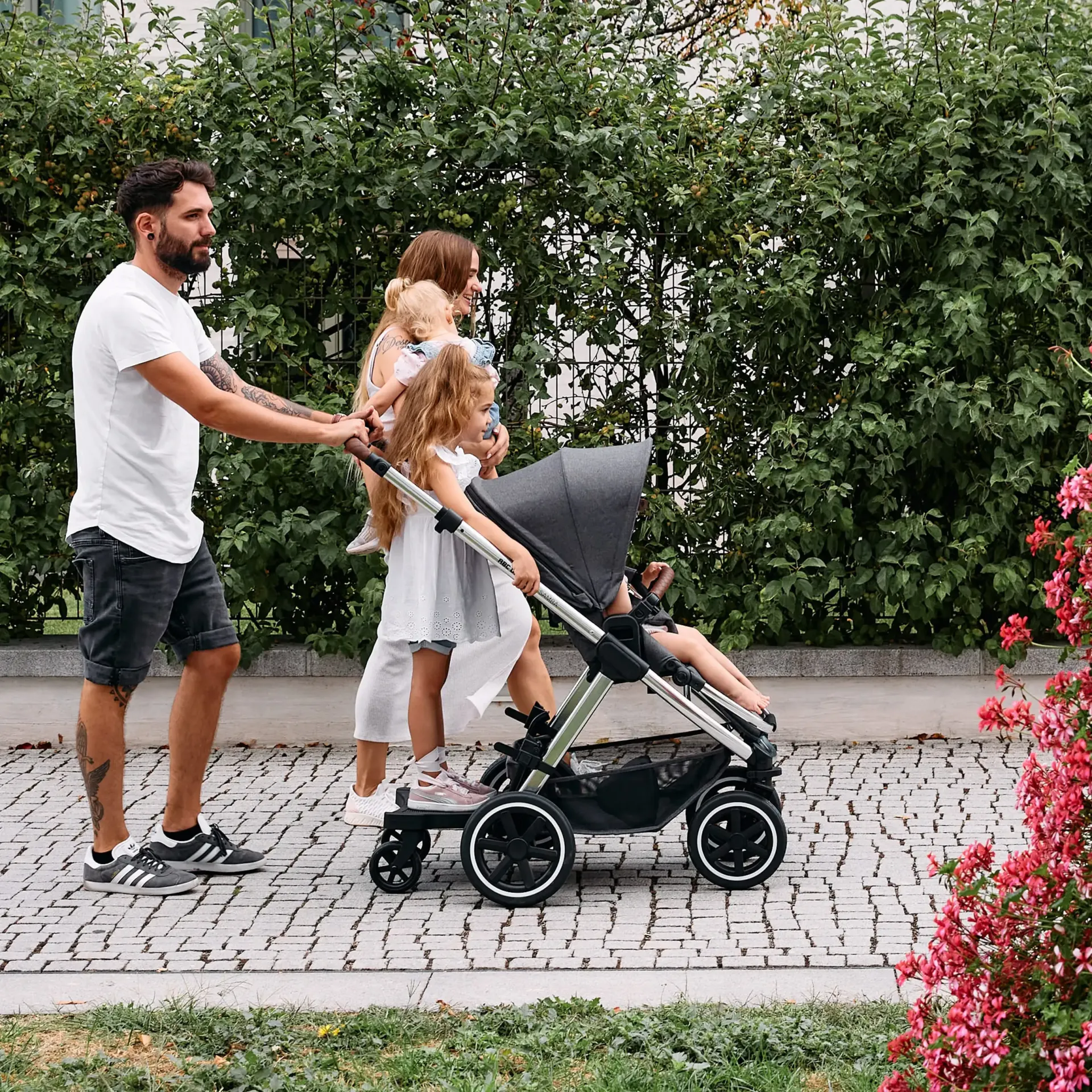 mann schiebt zwei kinder eins im buggy und eins auf dem montierten trittbett mann schiebt zwei kinder eins im buggy und eins auf dem montierten trittbett
