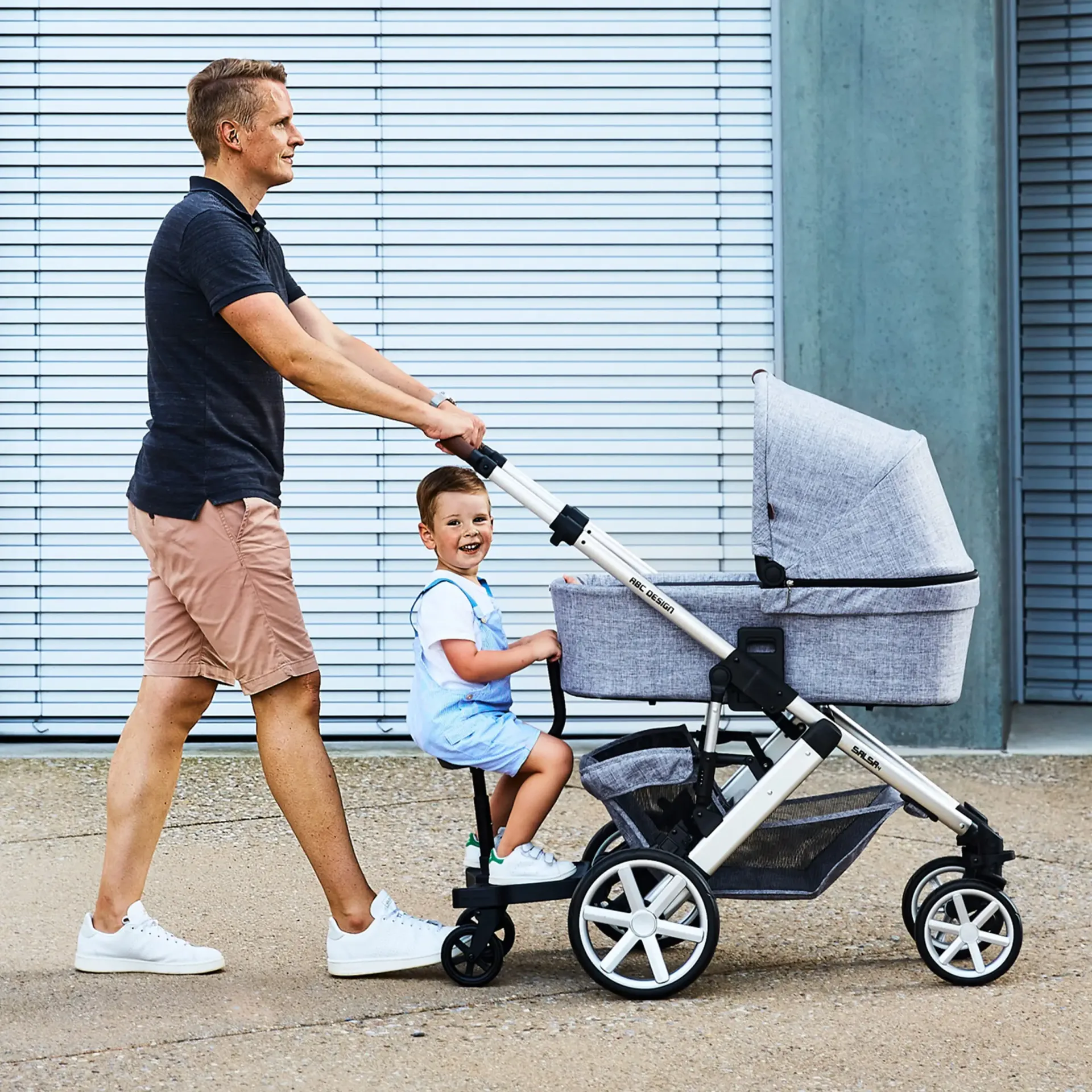 mann schiebt kind auf trittbrett mit sitz der am kinderwagen montiert ist mann schiebt kind auf trittbrett mit sitz der am kinderwagen montiert ist